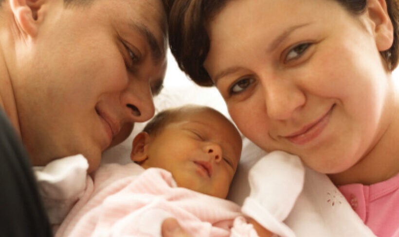 Smiling new parents head to head with sleeping infant between them