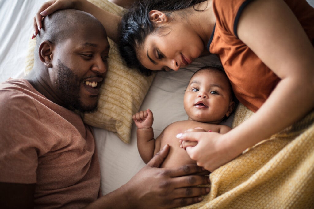 African American parents with infant daughter on bed, during a moment of family bonding time. Moments like these are crucial to the health and wellbeing of both parents and young children.